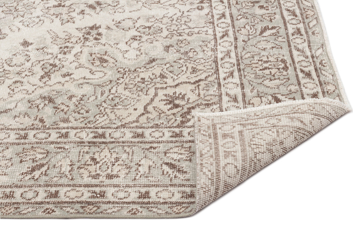 Beige and grey distressed rug with a traditional floral medallion pattern and a folded corner on a white background.