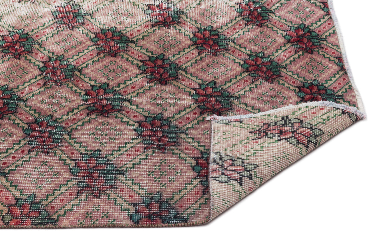 Pink and green vintage-style rug with a geometric diamond lattice pattern and floral motifs, shown with a corner folded.