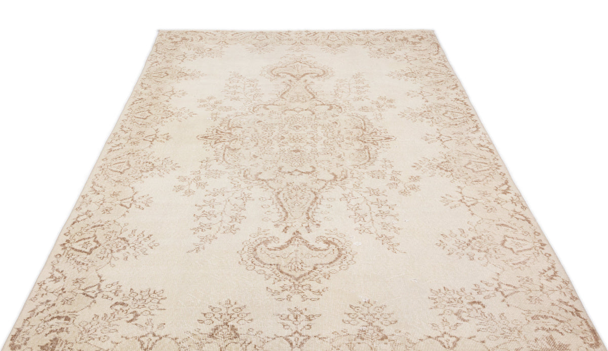 Cream and beige area rug with a faded traditional floral medallion pattern on a white background.
