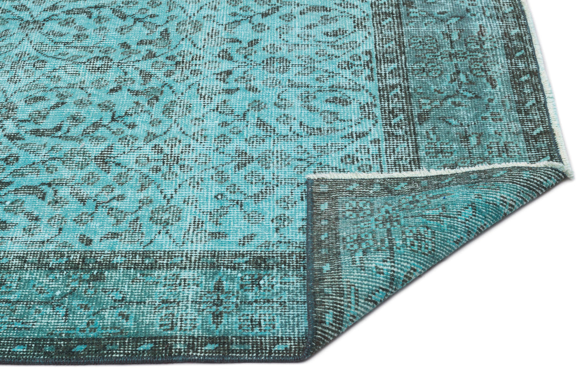 Turquoise and black distressed rug with a traditional floral medallion pattern and a folded corner.