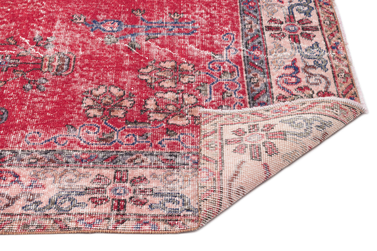 Distressed red Persian-style rug with floral motifs and a folded corner revealing a cream-colored backing.