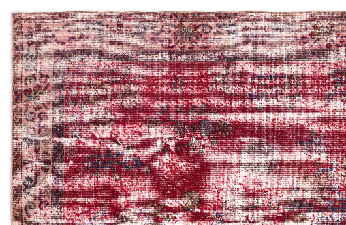 Distressed red rug with a faded floral medallion pattern and a decorative border in muted blue and pink tones.