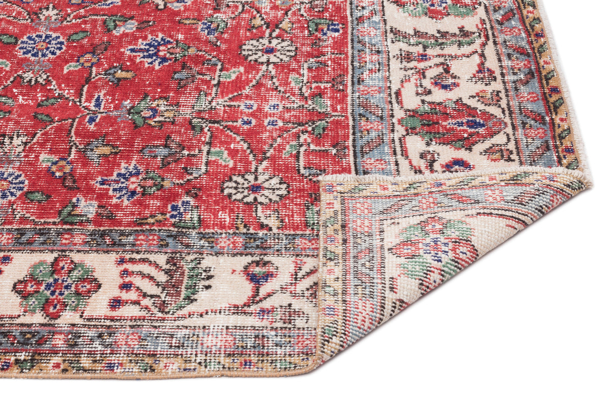 Red traditional rug with a floral medallion pattern, cream border, and distressed finish, shown with a folded corner.