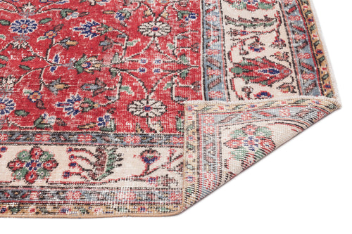 Load image 1 in gallery view. Red traditional rug with a floral medallion pattern, cream border, and distressed finish, shown with a folded corner.