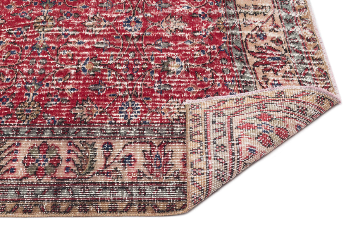 Red and beige traditional Persian-style rug with a floral medallion pattern and a folded corner on a white background.