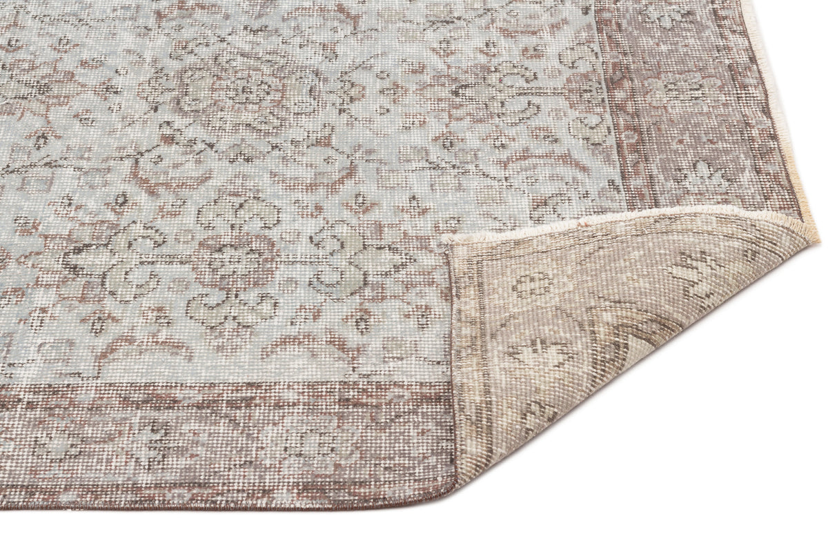 Light blue and brown distressed traditional rug with a floral medallion pattern and a folded corner on a white background.