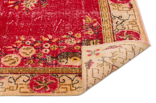 Load image 1 in gallery view. Distressed red rug with a floral pattern and beige geometric border, shown with a corner folded over on a white background.