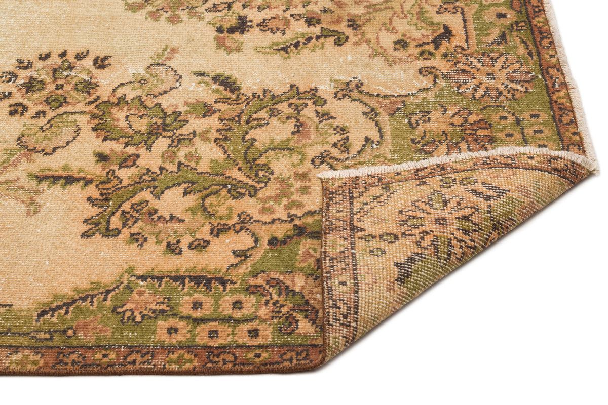 Tan and green vintage-style rug with a distressed floral pattern and a folded corner showing the woven backing.