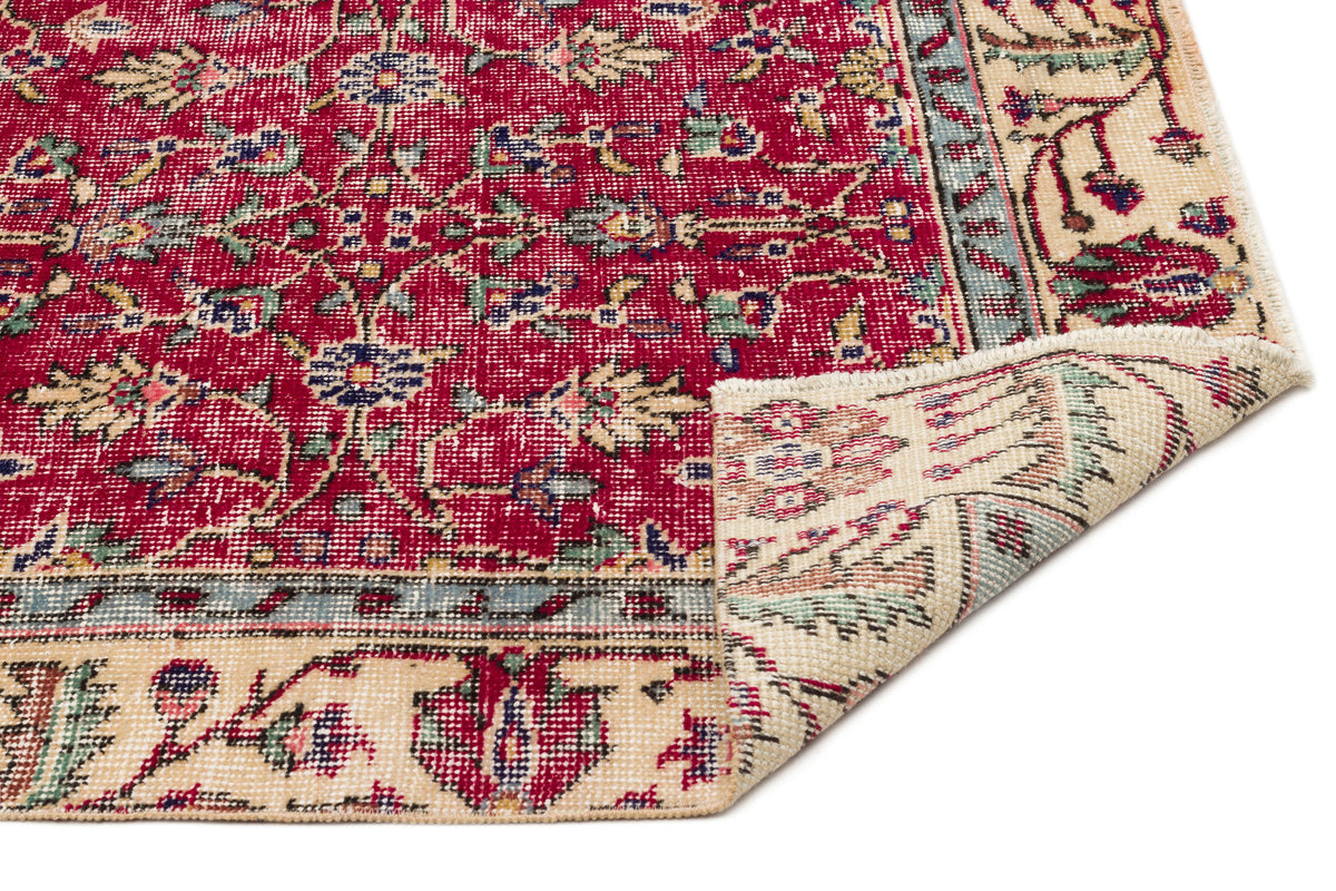 Red and cream traditional rug with a floral medallion pattern and a folded corner, isolated on a white background.