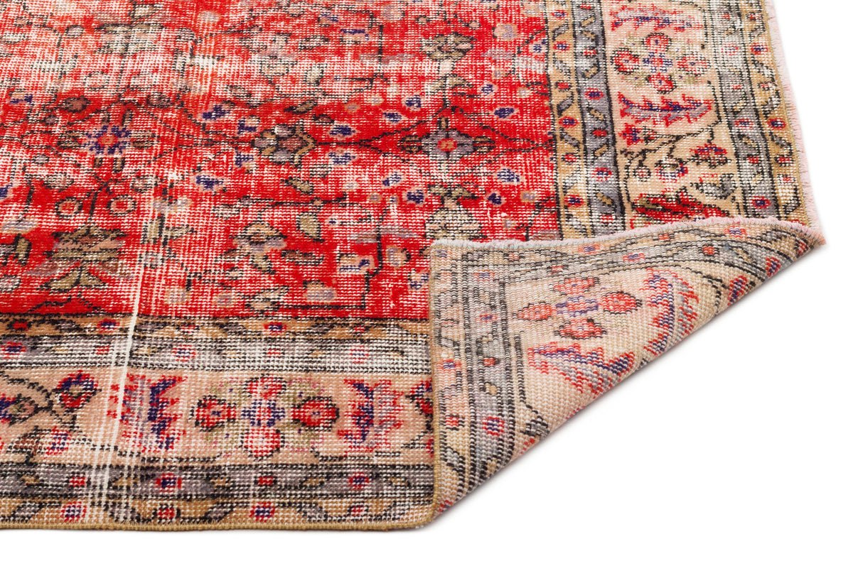 Red and beige vintage-style rug with a distressed floral medallion pattern, shown with a corner folded over.