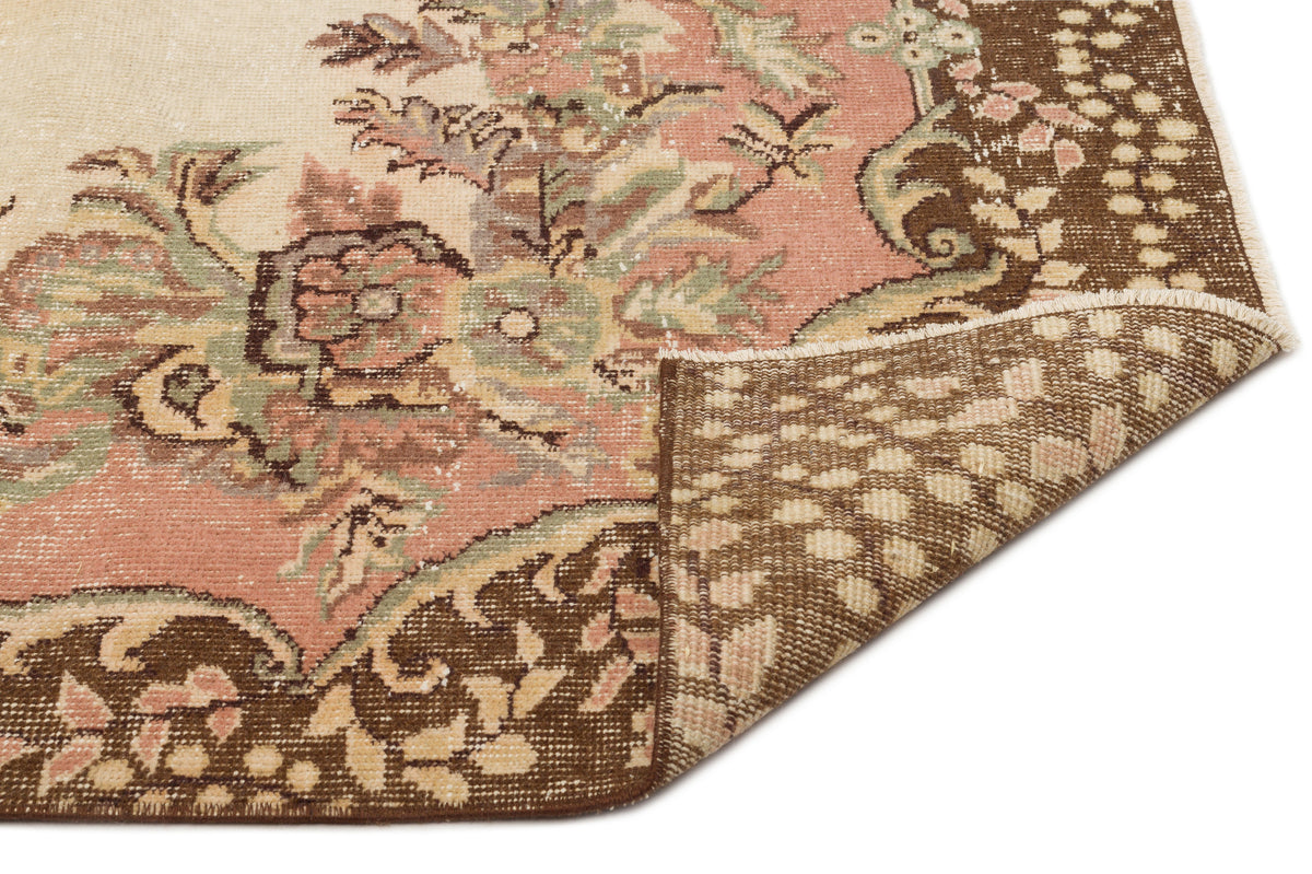Distressed floral rug in pink, brown, and cream with a folded corner revealing the woven backing.