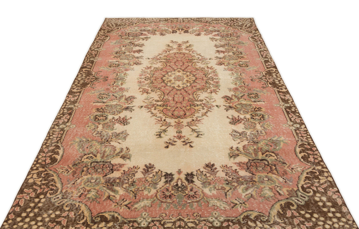 Cream, pink, and brown vintage-style rug with a central floral medallion and ornate border on a white background.