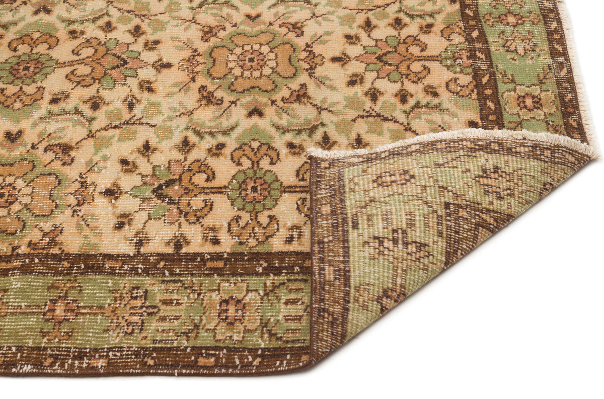 Tan, green, and brown traditional rug with a floral medallion pattern and a folded corner showing the underside.