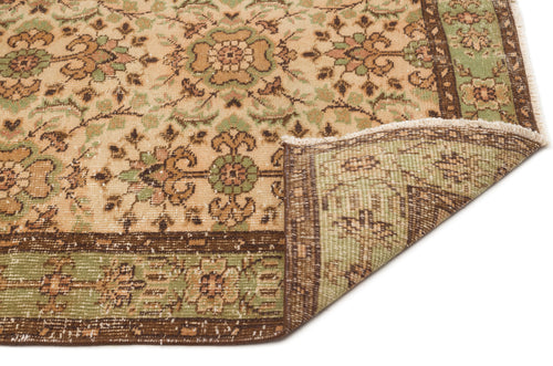 Load image 1 in gallery view. Tan, green, and brown traditional rug with a floral medallion pattern and a folded corner showing the underside.