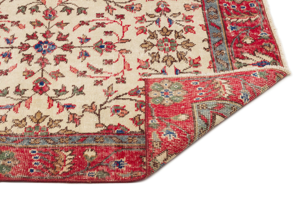 Cream rug with a red, blue, and green floral pattern and a folded corner revealing the underside.