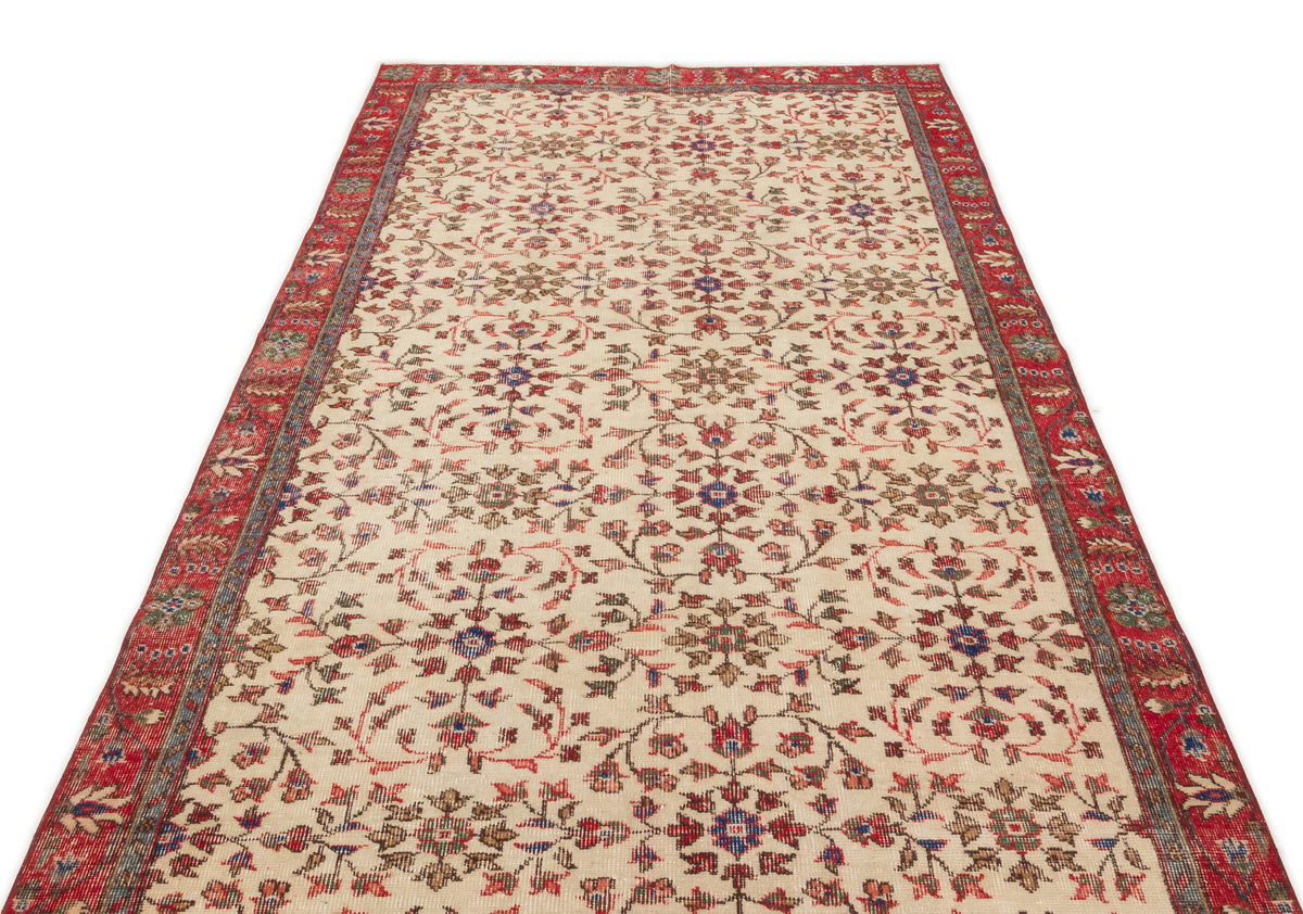 Cream area rug with a red border and a repeating floral medallion pattern in red, blue, and brown on a white background.