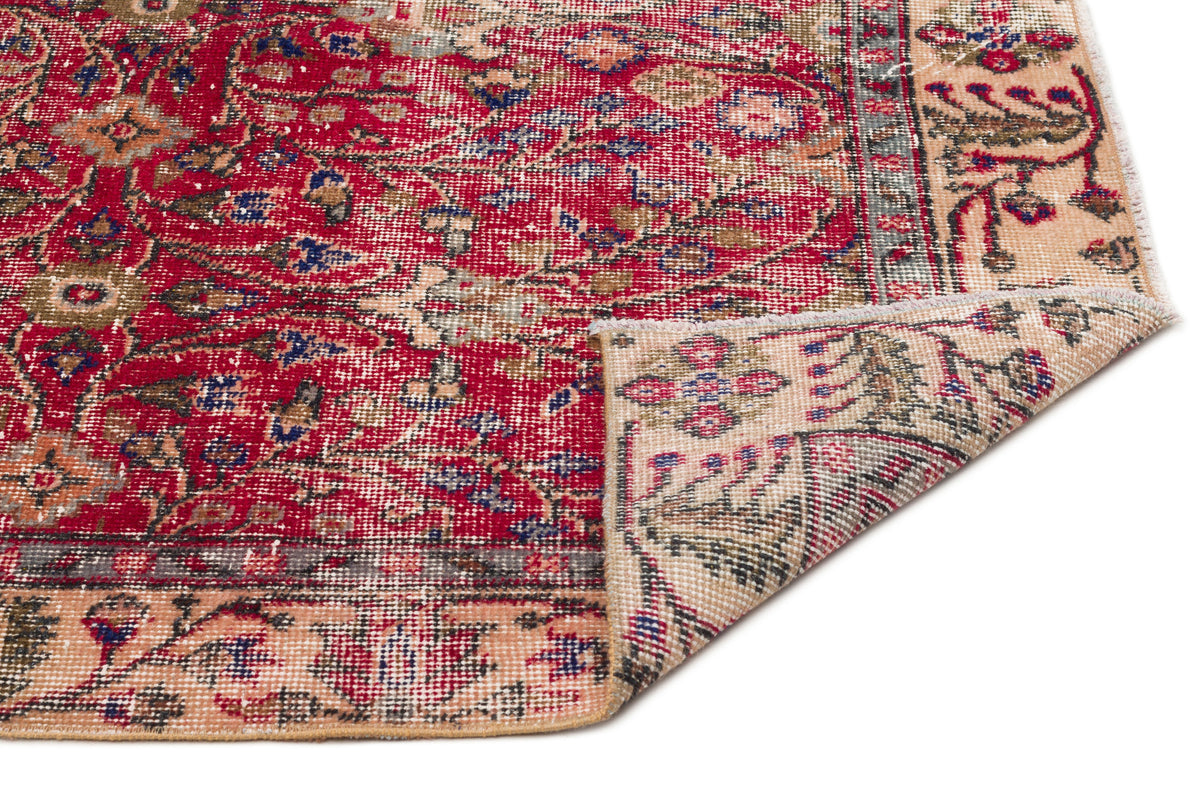 Red and beige traditional rug with a distressed floral medallion pattern and a folded corner, on a white background.