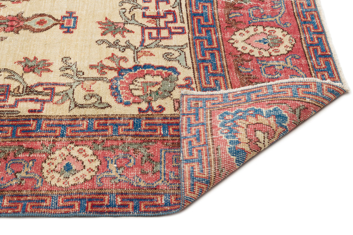 Cream, red, and blue traditional rug with a geometric border and floral motifs, shown with a corner folded over.