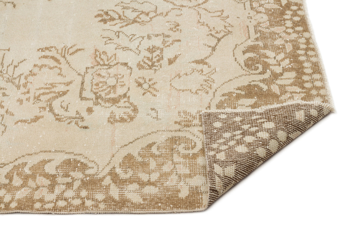 Beige and cream distressed rug with a traditional floral medallion pattern, shown with a folded corner on white.