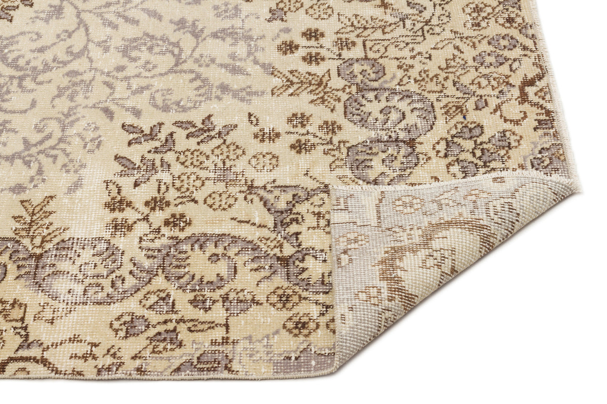 Beige and brown distressed floral medallion rug with a folded corner showing the woven backing.
