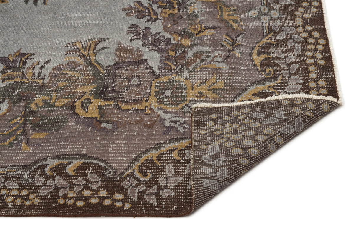 Distressed grey and brown rug with a floral medallion pattern and a folded corner showing the woven backing.