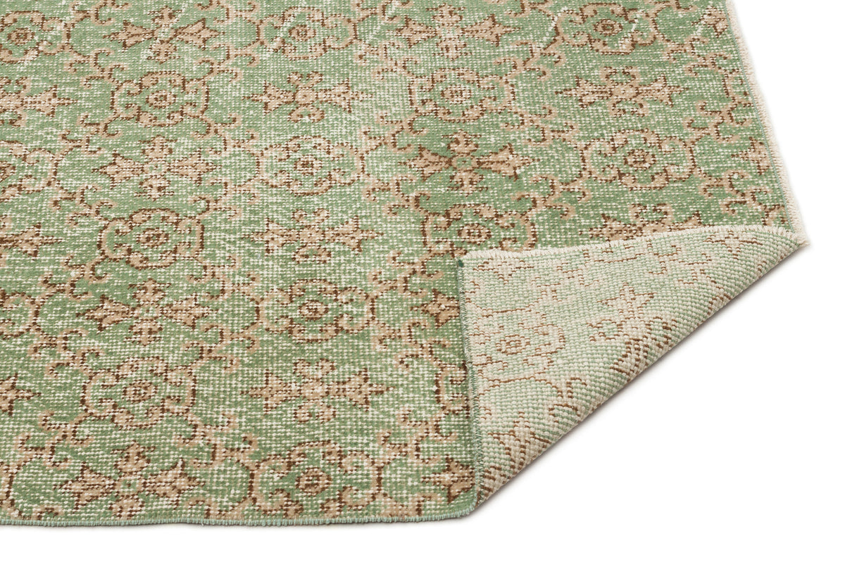 Sage green and beige rug with a repeating floral medallion pattern and a folded corner showing the woven backing.