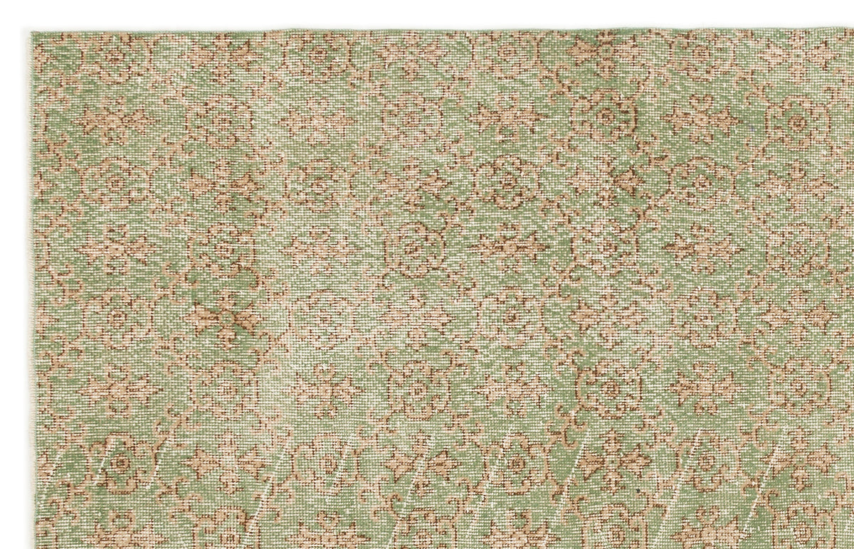 Sage green and beige rug with a repeating floral medallion pattern and a distressed, woven texture.