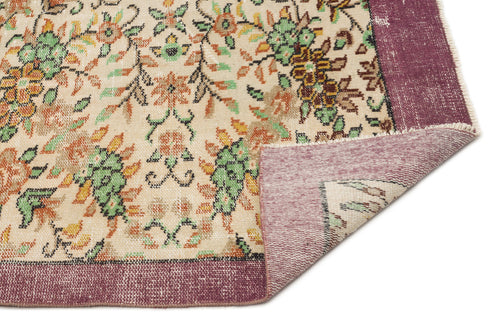 Load image 1 in gallery view. Cream rug with a floral pattern in green, orange, and black, featuring a wide purple border and a folded corner.