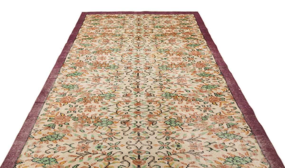 Beige vintage rug with a floral pattern in orange and green, featuring a solid dark purple border.