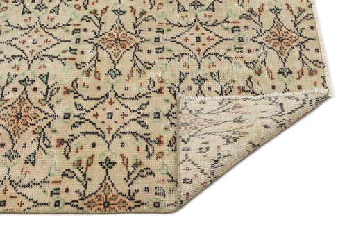 Load image 1 in gallery view. Beige vintage-style rug with a black, green, and rust floral medallion pattern and a folded corner showing the backing.