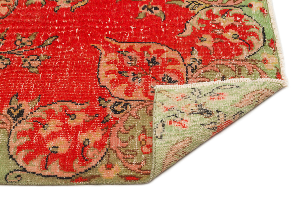 Distressed red and sage green floral medallion rug with a folded corner showing the reverse side on a white background.