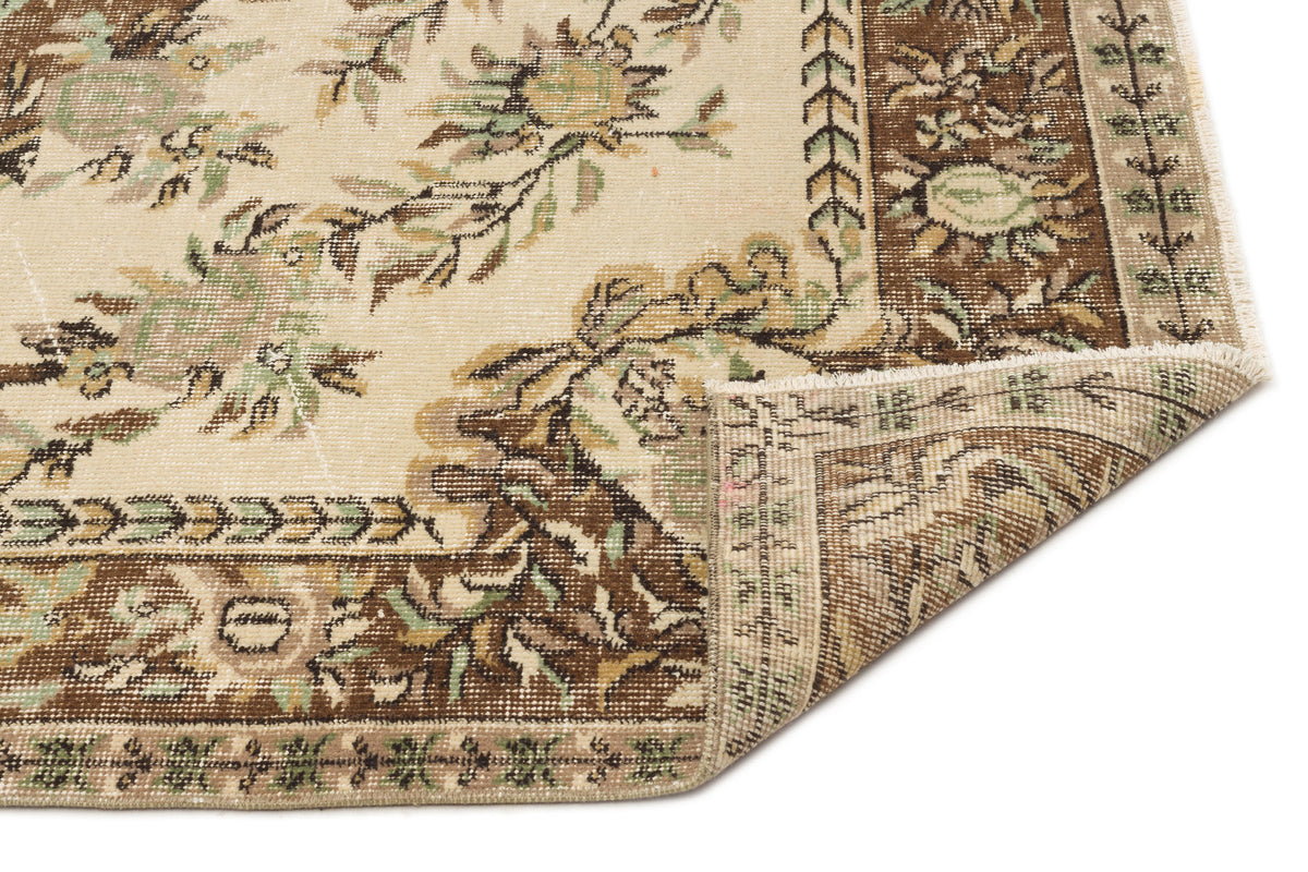 Beige, brown, and sage green traditional floral rug with a folded corner showing the woven backing.
