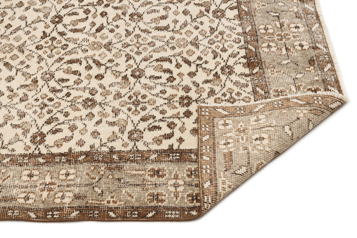 Cream and brown traditional rug with a floral medallion pattern and a folded corner showing the woven backing.