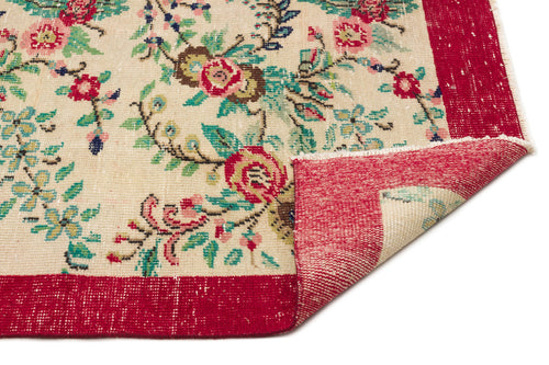 Load image 1 in gallery view. Cream rug with a floral pattern in red, green, and blue, featuring a wide red border and a folded corner.