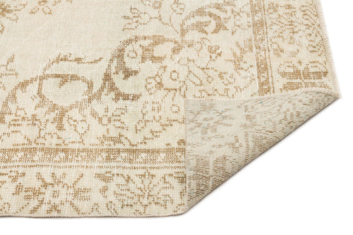 Load image 1 in gallery view. Beige and cream distressed traditional rug with a floral medallion pattern, shown with a corner folded over.
