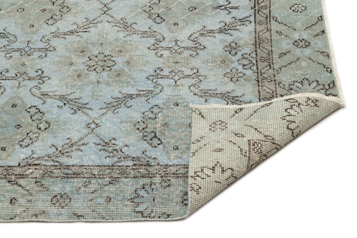 Light blue and grey traditional rug with a distressed floral medallion pattern, shown with a corner folded over.