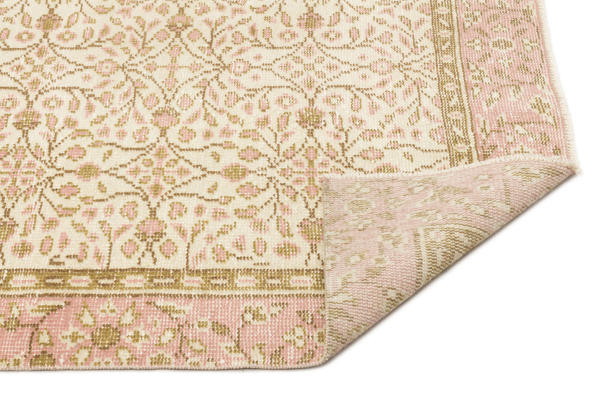 Cream, pink, and tan rug with a traditional floral pattern and a folded corner, isolated on a white background.