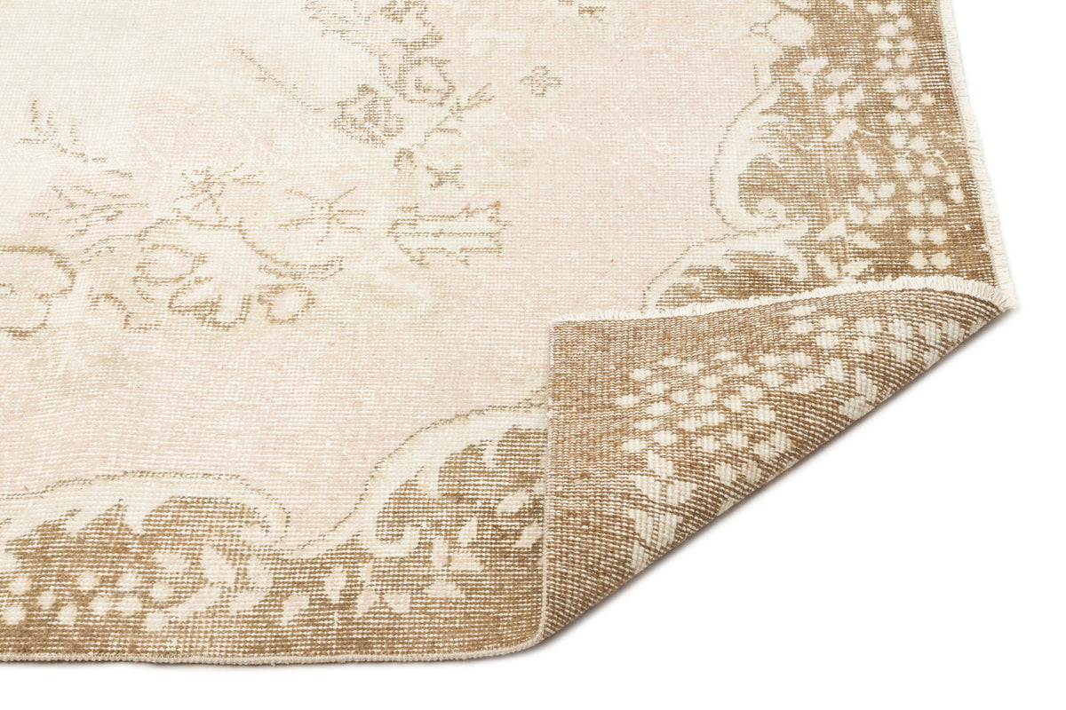 Beige and cream vintage-style rug with a faded floral medallion pattern and a folded corner, isolated on white.