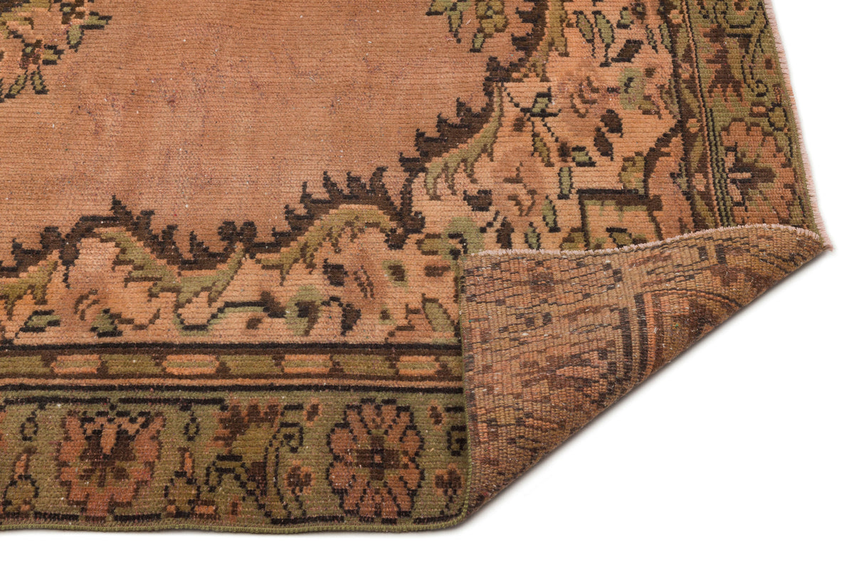 Terracotta and olive green vintage-style rug with a floral medallion border, shown with a corner folded over.