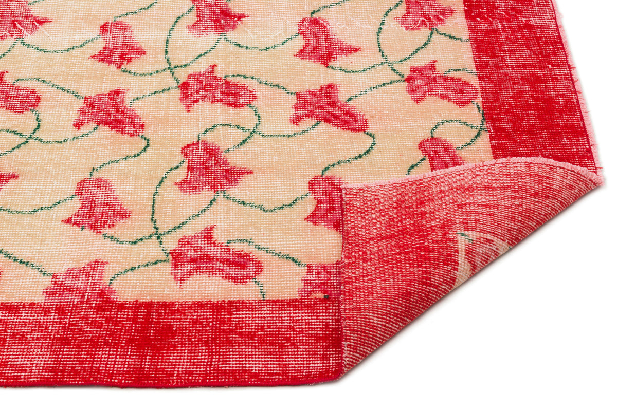 Beige rug with red floral motifs, green vines, and a solid red border, shown with a corner folded over.
