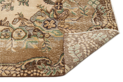 Load image 1 in gallery view. Distressed brown and beige rug with a traditional floral medallion pattern, shown with a corner folded over.