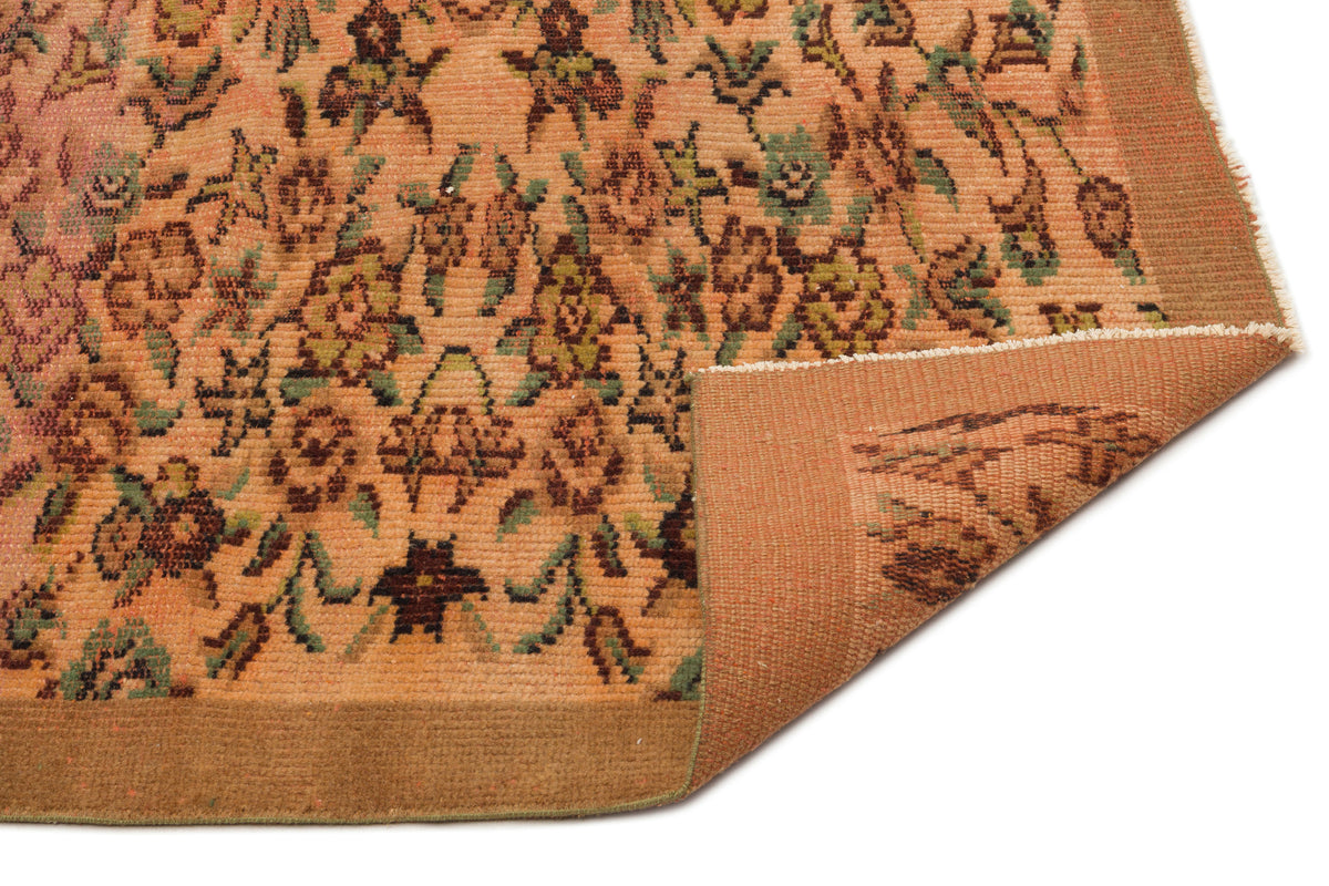 Peach and brown traditional rug with a floral pattern and a folded corner showing the plain backing.