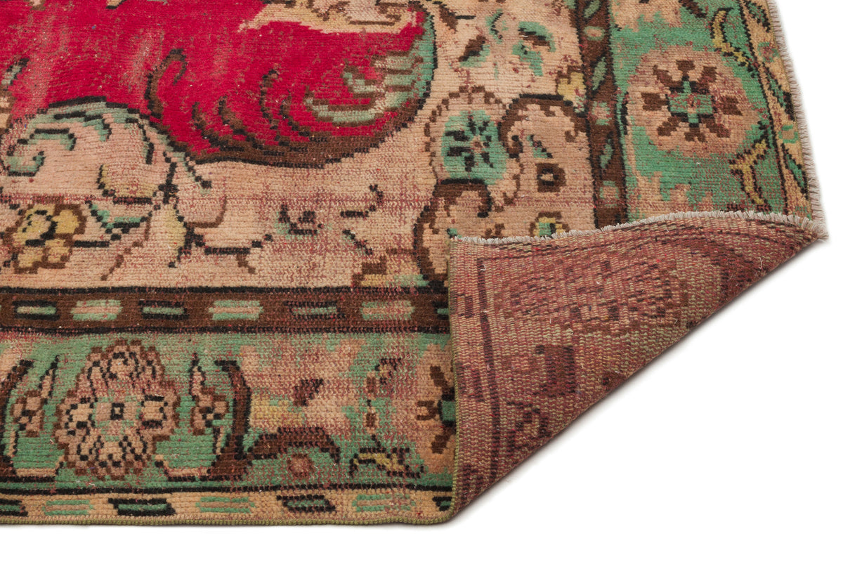 Distressed vintage-style rug with red, green, and beige floral patterns, shown with a corner folded over.