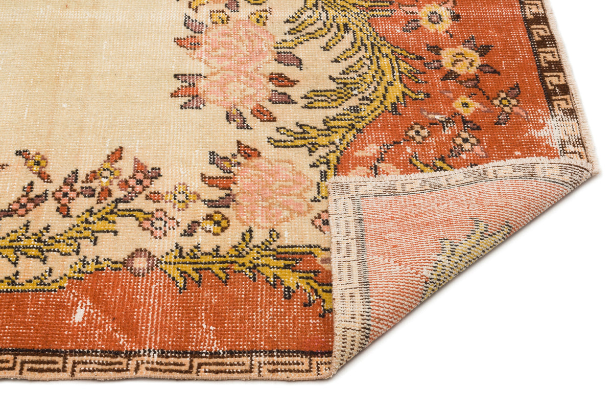 Distressed cream and rust-orange rug with a floral medallion pattern and a folded corner showing the woven backing.