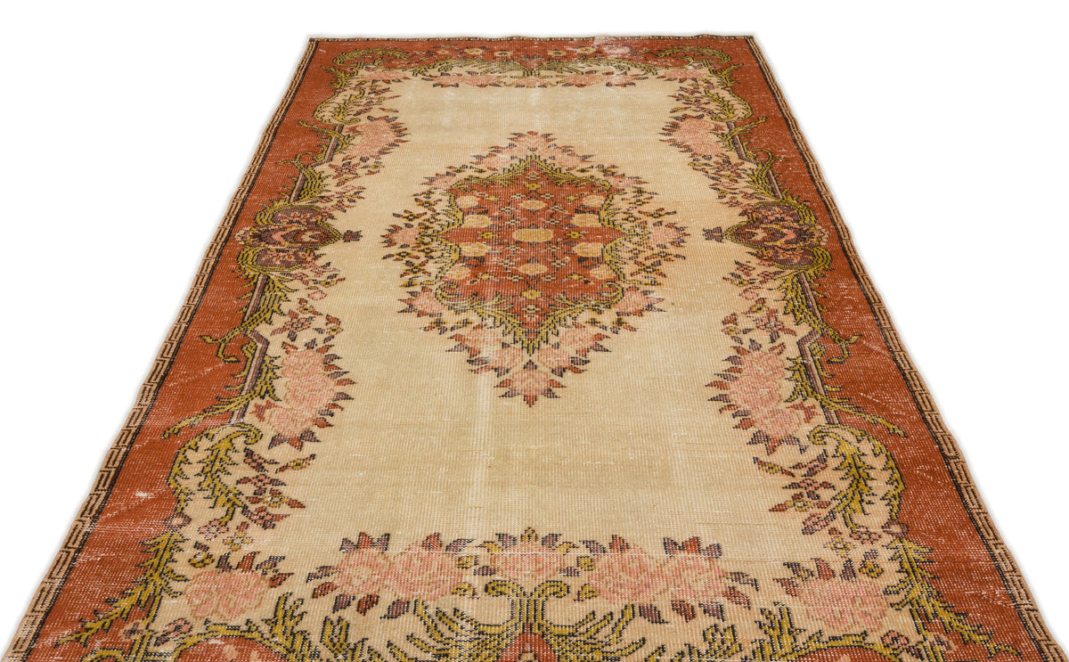 Distressed beige rug with a central rust-colored medallion and floral border in shades of pink, green, and brown.