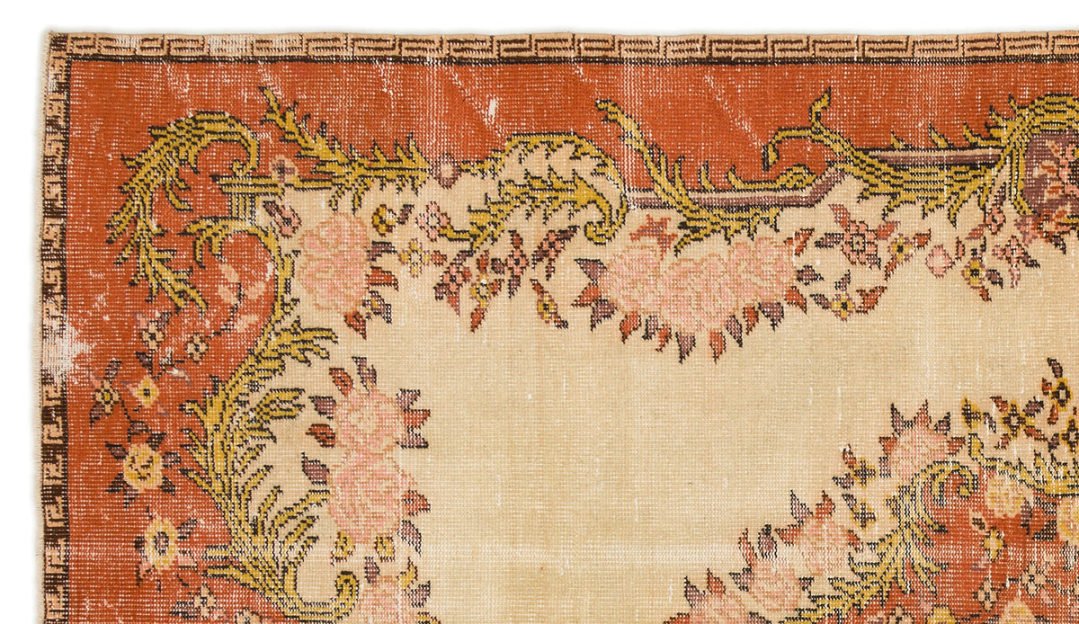 Terracotta and beige vintage-style rug with a floral border, geometric edge detail, and distressed texture.