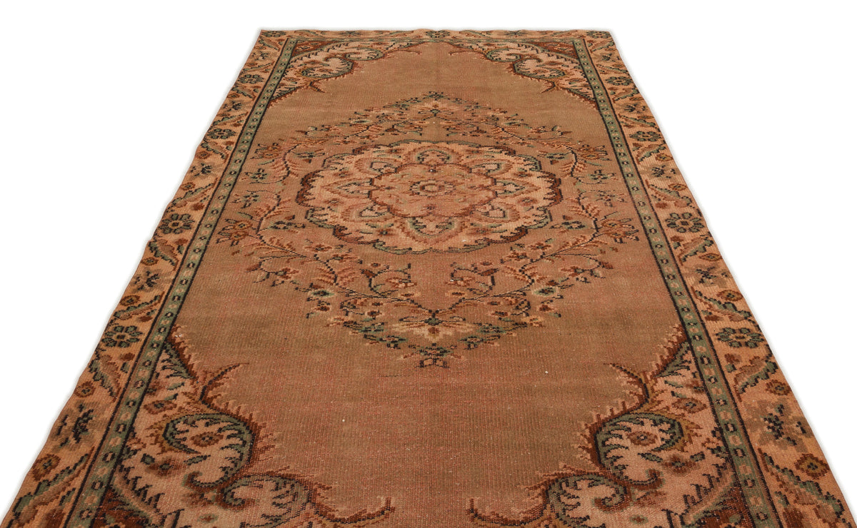 Distressed terracotta rug with a central floral medallion and ornate border in muted green and brown tones.