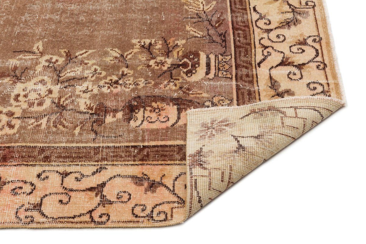 Brown and beige vintage-style rug with a distressed floral pattern and a folded corner revealing the woven backing.