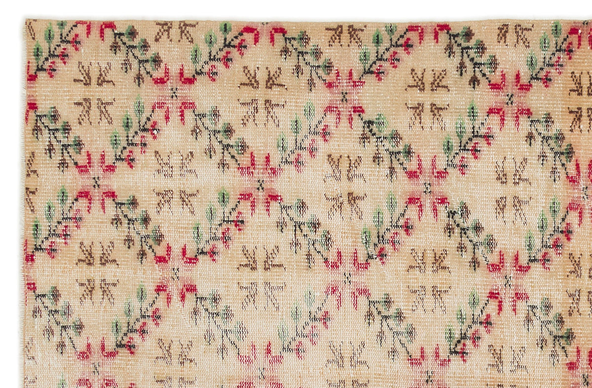 Tan rug with a repeating diamond lattice pattern featuring red, green, and black floral vine motifs.