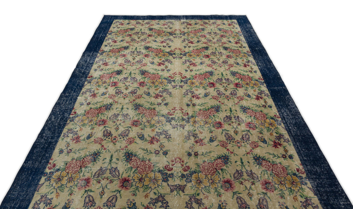 Beige rug with a distressed floral pattern in red, yellow, and blue, featuring a wide navy blue border.